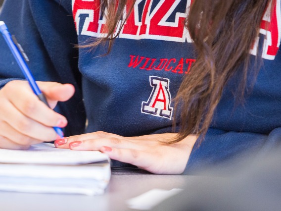 Student in UArizona pullover writing in a notebook