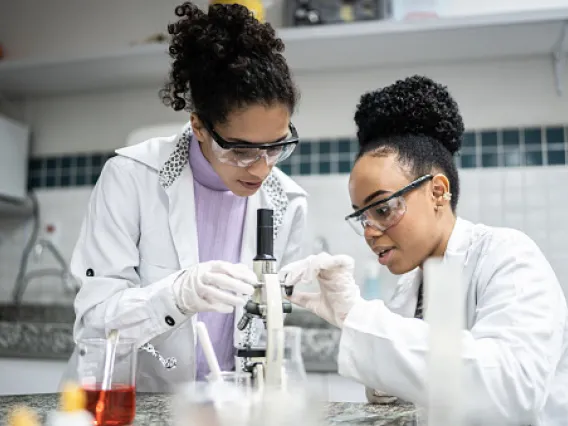 Women in lab coats staring at microscope