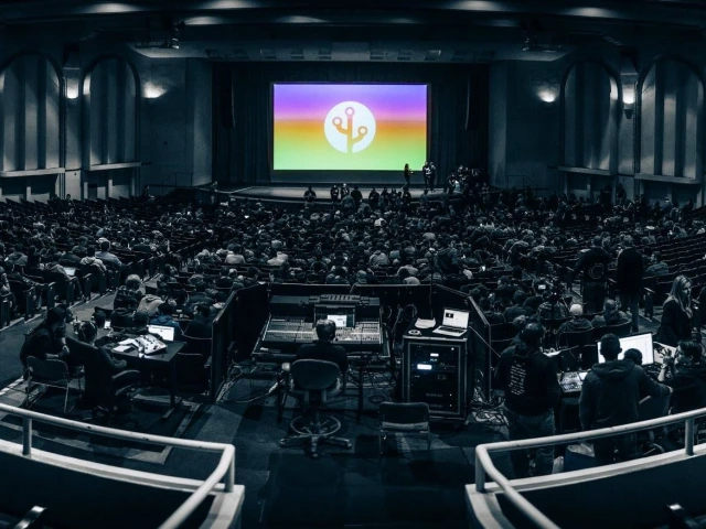 An auditorium filled with  people waiting on a presentation to begin.