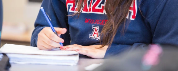 Student in UArizona pullover writing in a notebook